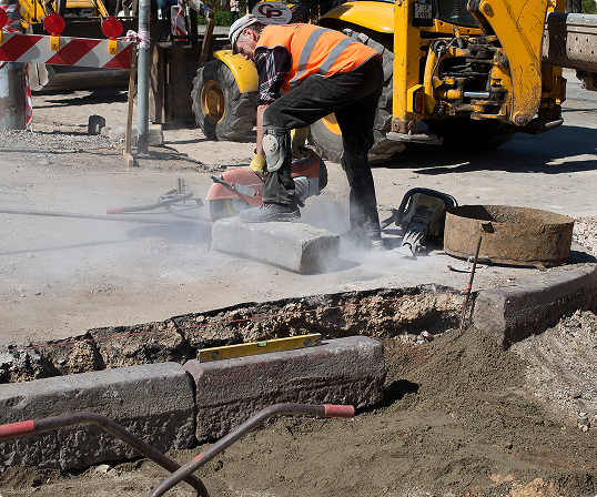 A professional man works on asphalt maintenance with professional equipment and construction machinary in the background