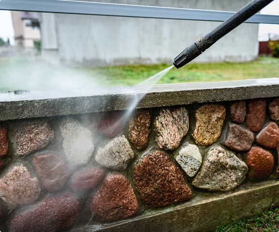 A professional pressure washer pointed at a stone wall getting cleaned