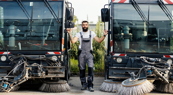 Profesional power sweeping worker standing between two sweeper trucks