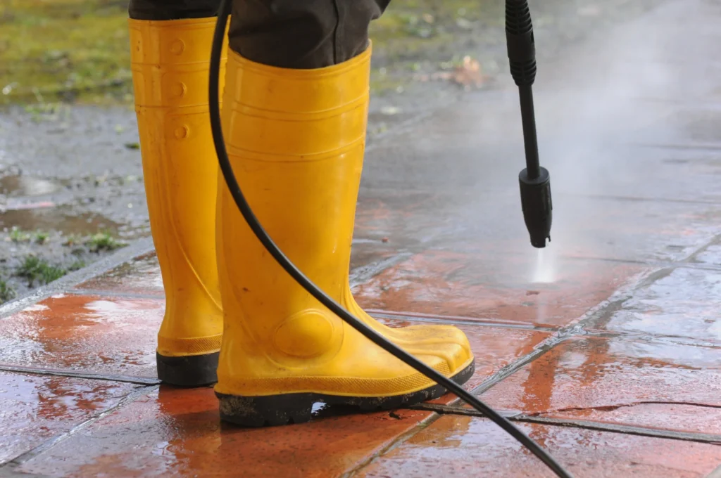 Close-up-of-a-persons-legs-using-high-pressure-cleaning-equipment-to-wash-city-sidewalk-tiles-scaled