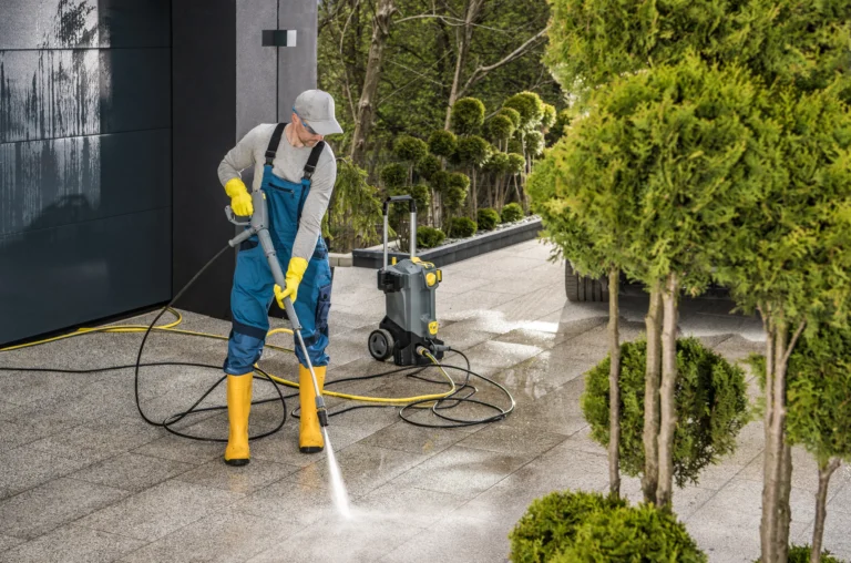 Worker-in-uniform-using-a-pressure-washer-to-clean-sidewalk-tiles-next-to-a-commercial-garage-in-the-city-scaled