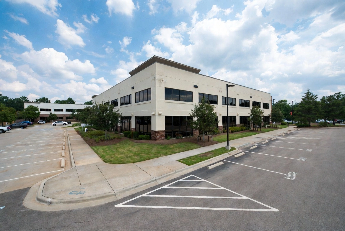 Modern two-story office building with large parking lot under a blue sky with clouds