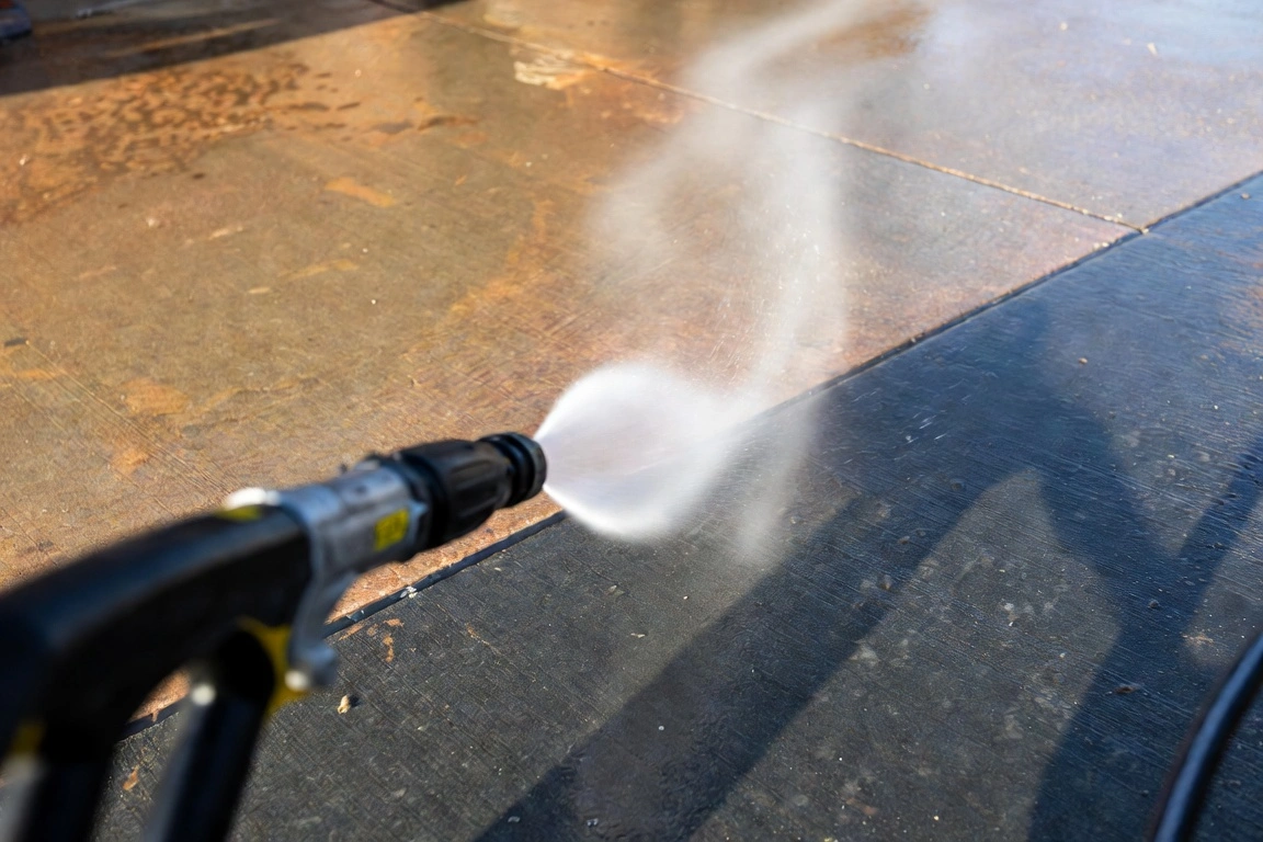 Close-up of pressure washer nozzle spraying water onto dirty pavement