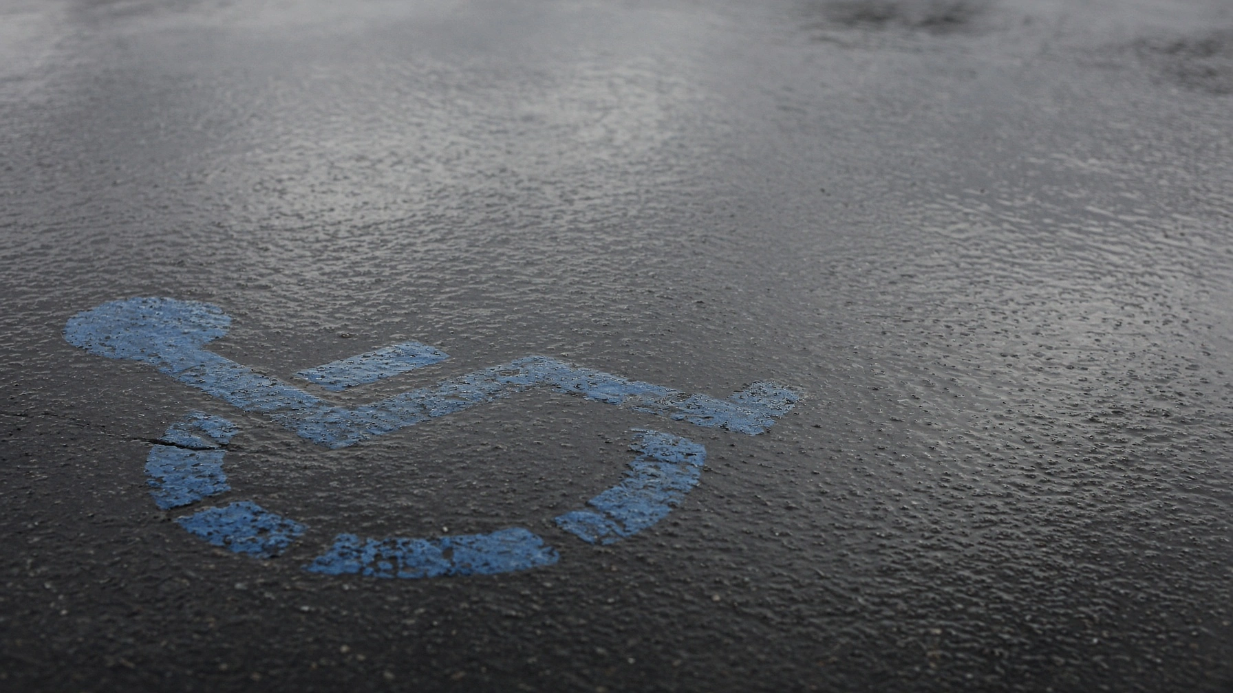 Faded handicap parking symbol on wet, icy asphalt